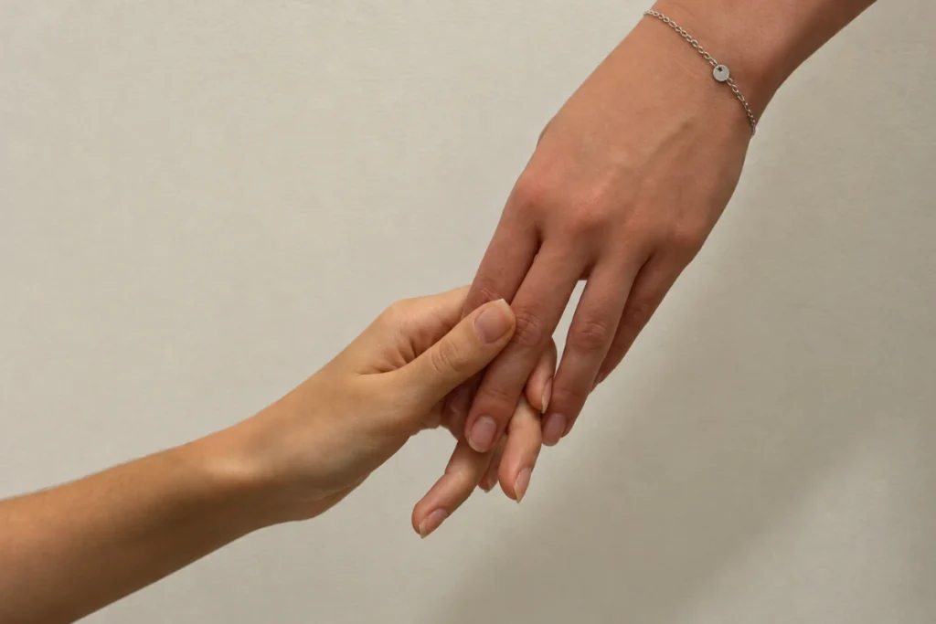 Primer plano de dos personas que entrelazan suavemente sus manos en un gesto de apoyo emocional, una de ellas con una pulsera plateada.
