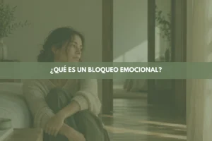 Mujer sentada en un sofá con las piernas recogidas y la mirada perdida hacia una ventana, representando un bloqueo emocional.